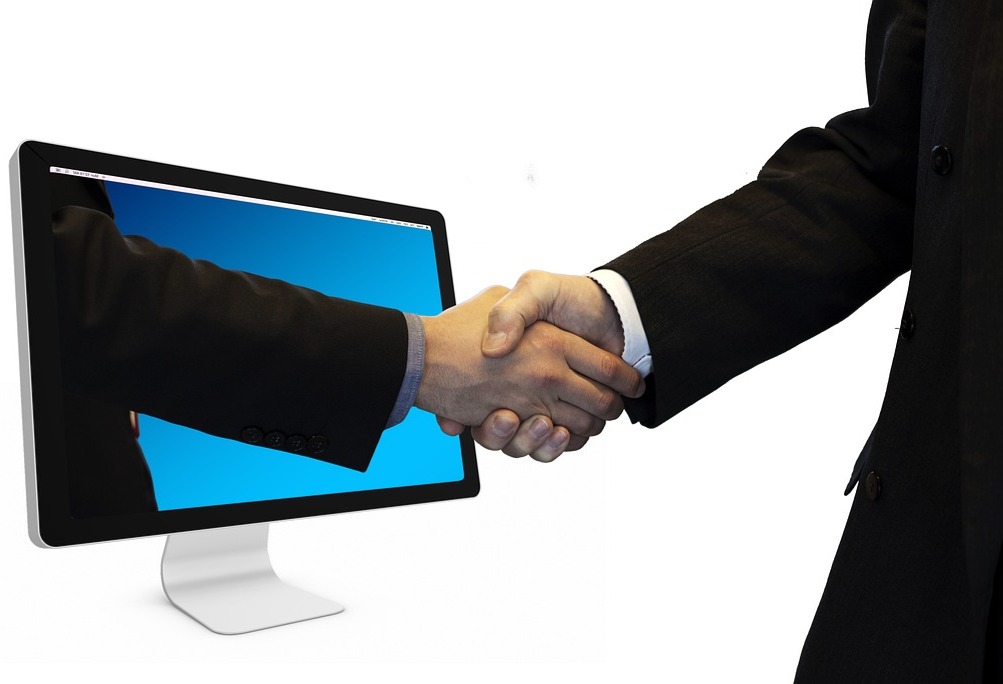 Händedruck durch Computerbildschirm – Symbol für digitale Partnerschaft und Online-Zusammenarbeit. Händedruck zwischen zwei Geschäftspartnern, symbolisch durch einen Computerbildschirm, als Zeichen für digitale Zusammenarbeit und erfolgreiche Online-Geschäftsbeziehungen.