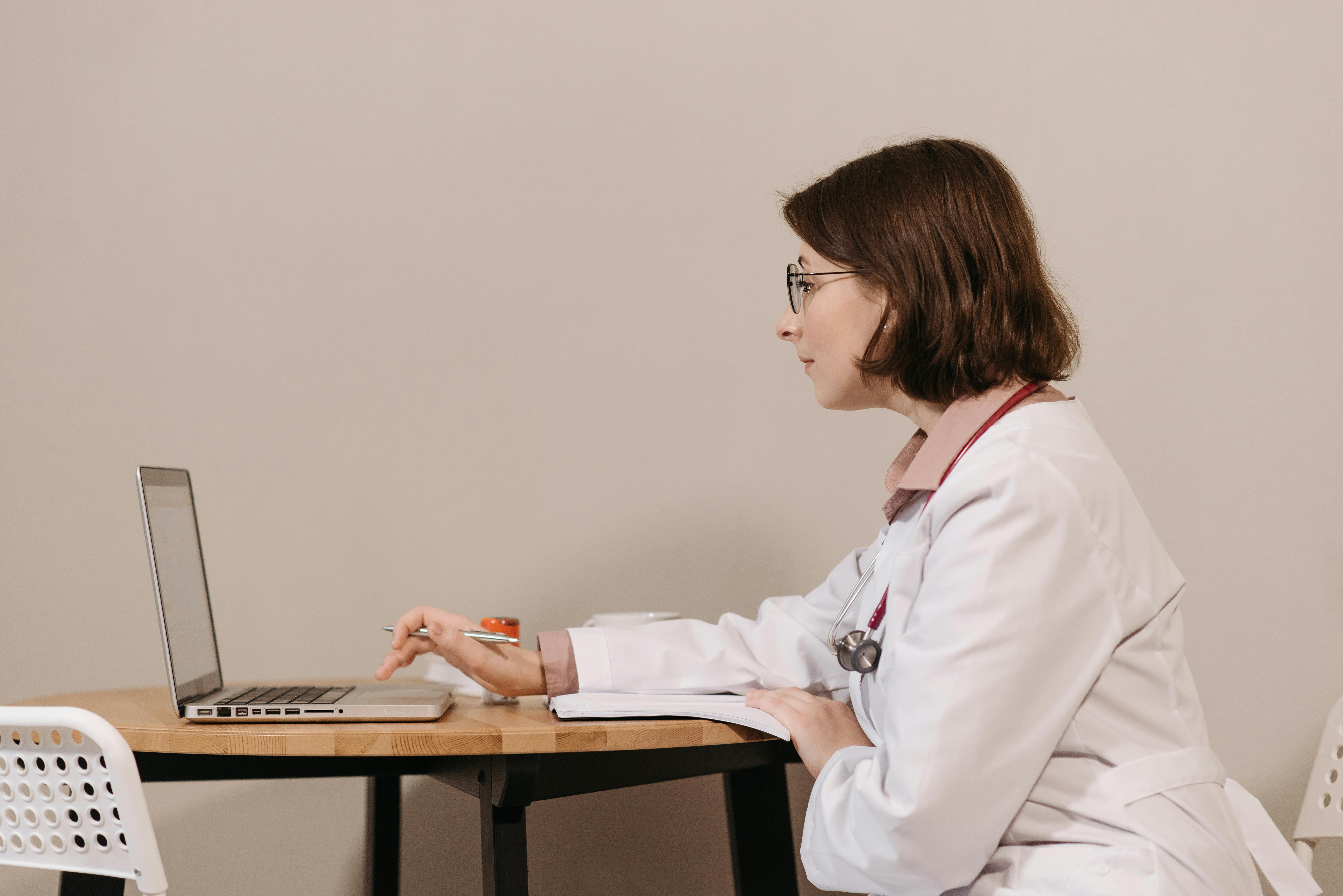 Professionelle Praxis-Webseite – Webdesign für den Gesundheitsbereich Arzt mit Brille und Stethoskop sitzt am Schreibtisch und betrachtet die Webseite einer Arztpraxis auf seinem Laptop – moderne Online-Präsenz und digitale Patienteninformation im Gesundheitswesen.
